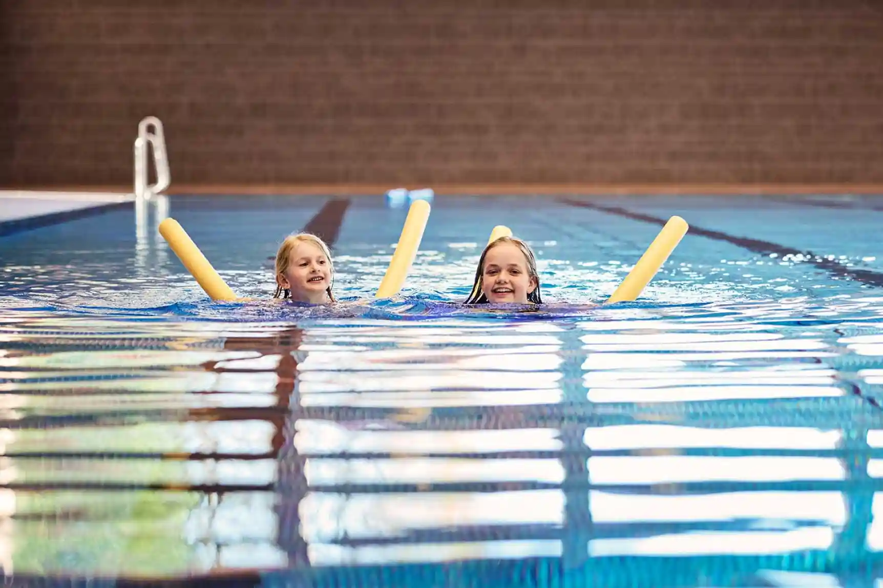 Zwei Mädchen schwimmen im Wasser mit einer gelben Poolnudel