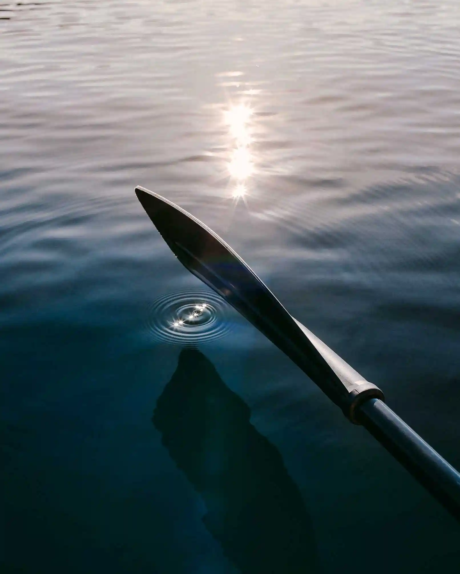 Ein Teil vom Paddle berührt sanft das Wasser, in dem sich die Sonnenstrahlen spiegeln